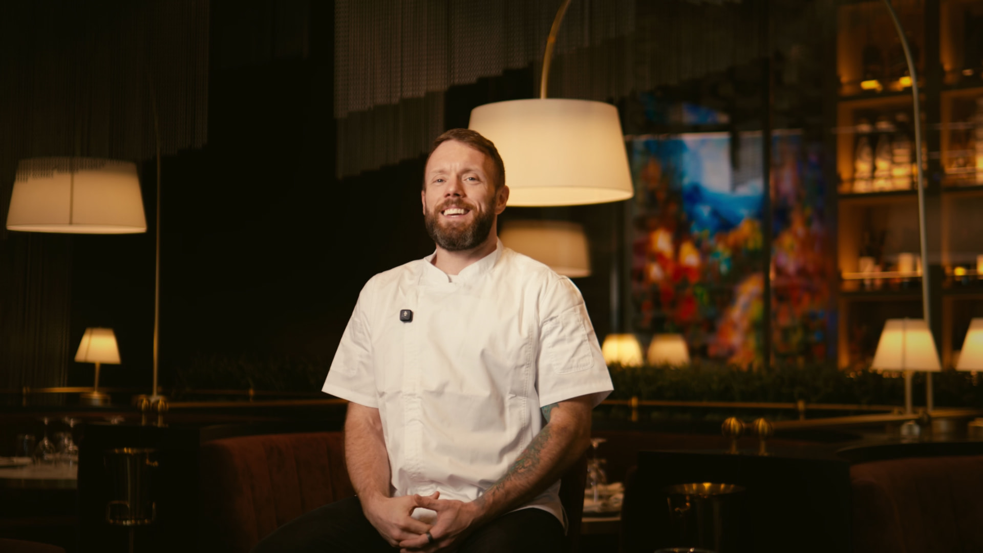 Chef in white jacket seated in a warmly lit restaurant dining room